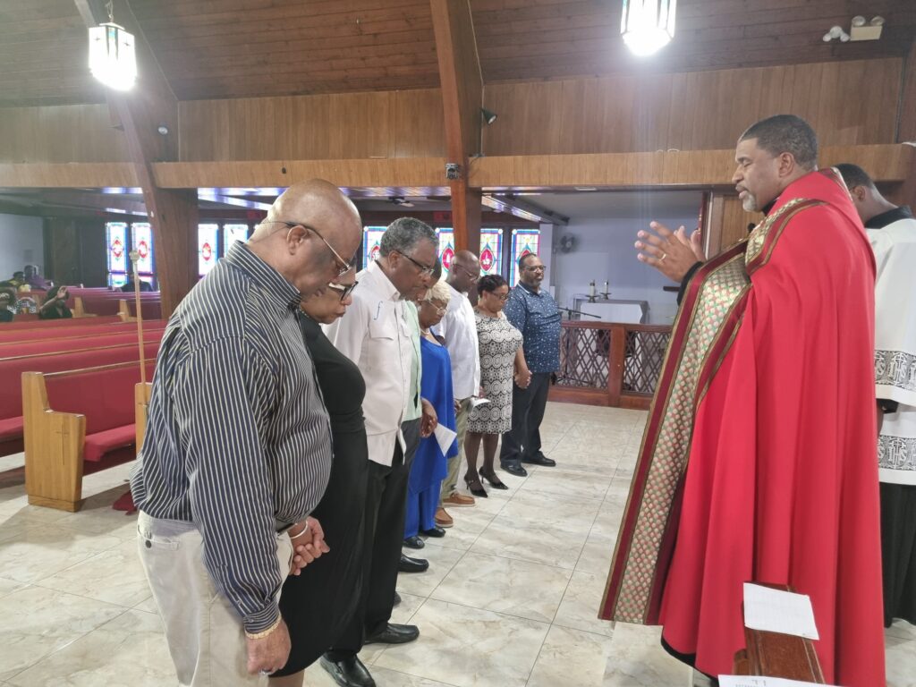 Seen in photo, Father Kirkland H. Russell, Jr., Rector of the Pro-Cathedral of Christ The King, Freeport, offers prayers and blessings for Minister Mitchell and team members of the Passport Office and Immigration Department, Grand Bahama.